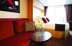 Celebrity Silhouette - Celebrity Cruises - Dekorativní květiny na dřevěném stolku a červené luxusní sofa v suite kajutě