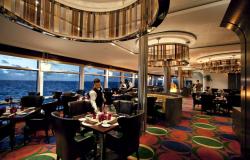 Celebrity Solstice - Celebrity Cruises - číšník upravující stůl v luxusní restauraci na lodi s výhledem na okolní moře